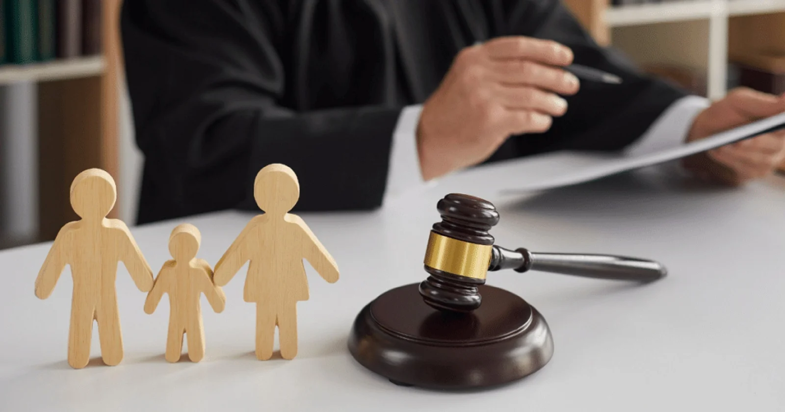 Wooden figurines of a family holding hands on a judge's desk beside a gavel