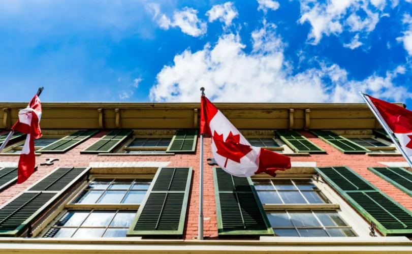 Canadian flags flying outside a red-brick building against a blue sky