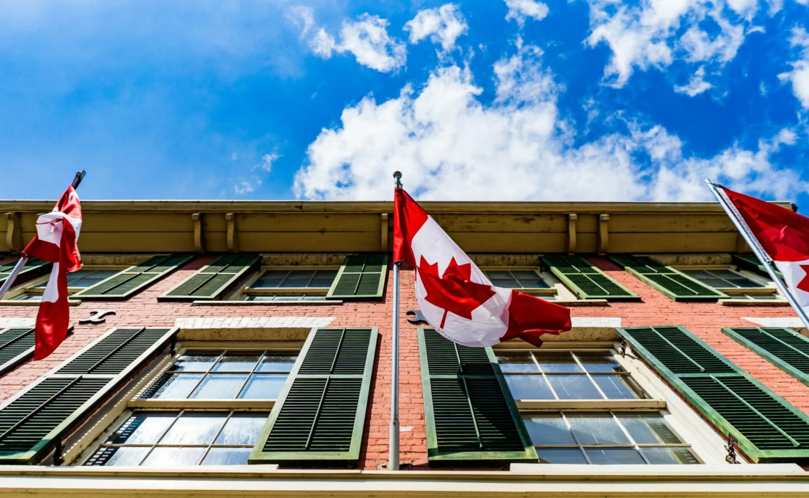 Canadian flags flying outside a red-brick building against a blue sky