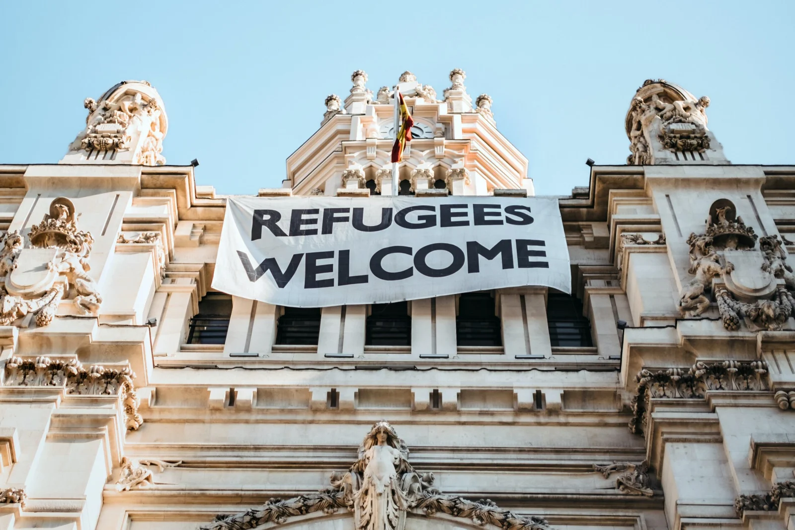 A large 'Refugees Welcome' banner hanging on the facade of an ornate stone building
