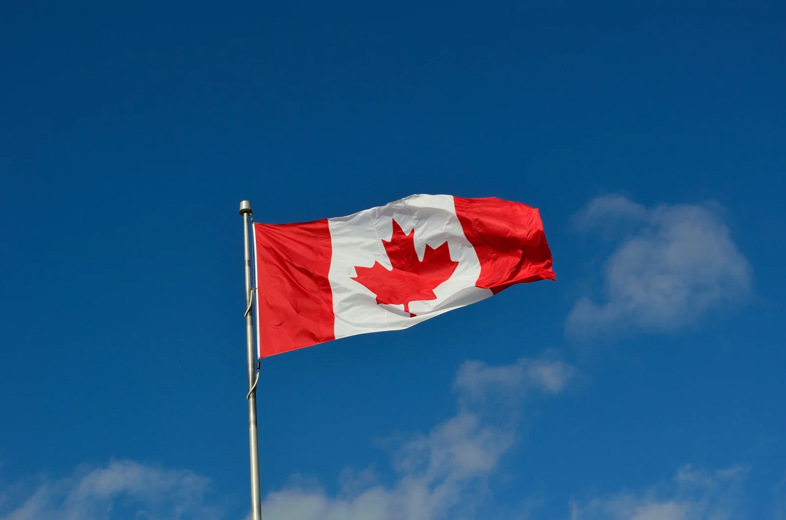 Canadian flag waving on a flagpole against a clear blue sky